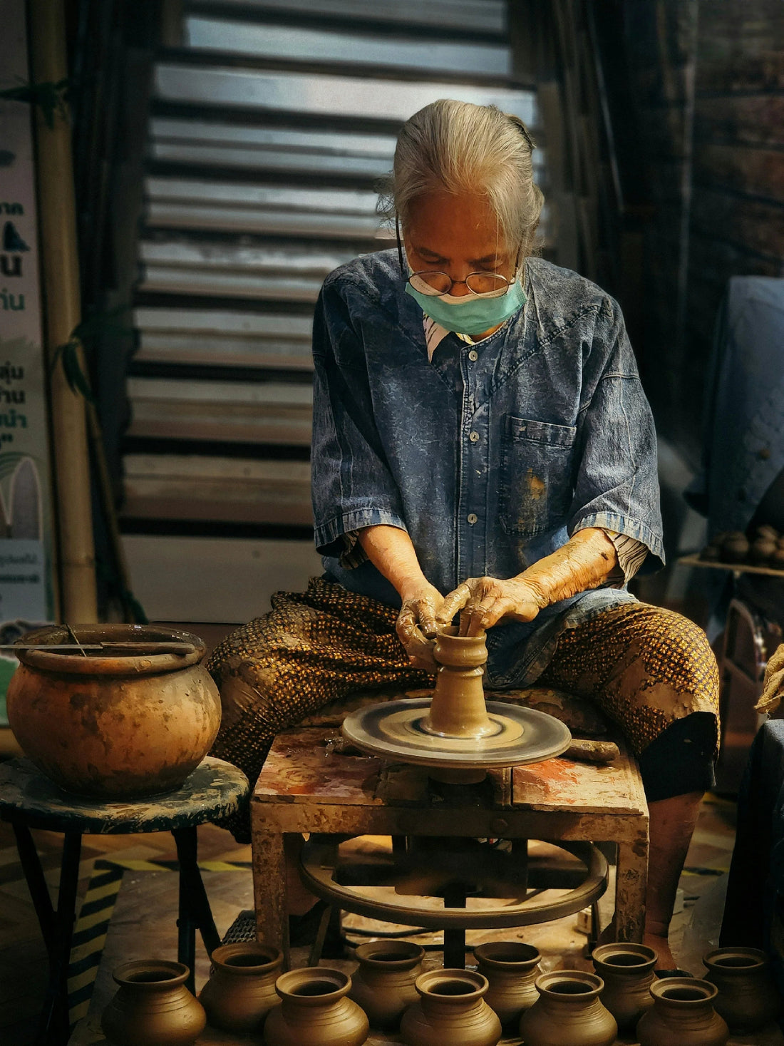 Artisan shaping clay pottery on a spinning wheel, surrounded by handmade ceramic pots.