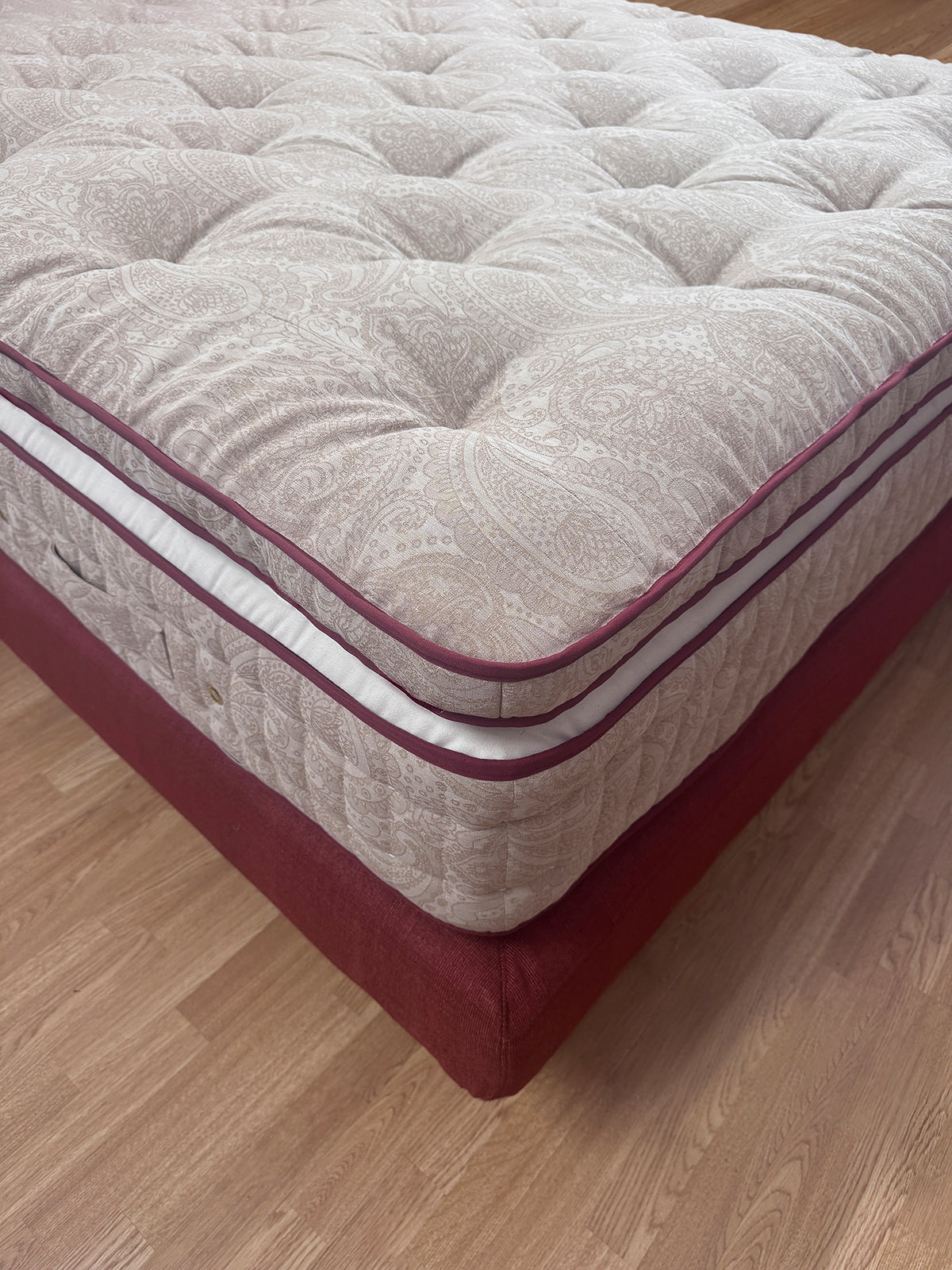 Close-up of a luxury tufted mattress with paisley pattern and red side panels on wooden floor