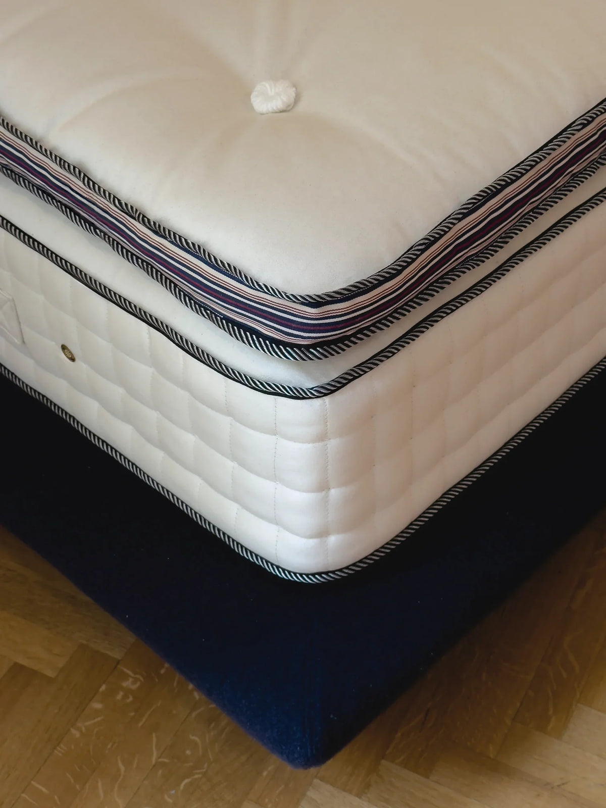 Dettaglio di un materasso di lusso fatto a mano, con tessuto bianco trapuntato e bordo a righe, sul suo boxspring