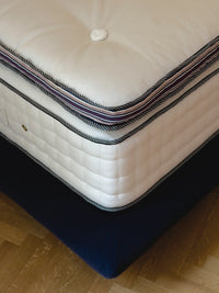 Dettaglio di un materasso di lusso fatto a mano, con tessuto bianco trapuntato e bordo a righe, sul suo boxspring